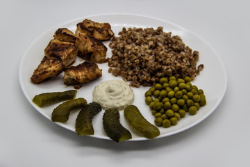 Delicious buckwheat porridge with chicken, green peas, cucumbers and sauce on a white plate. Tasty chicken skewers from fillet on a white plate. Healthy and tasty  food with chicken meat.