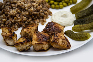 Delicious buckwheat porridge with chicken, green peas, cucumbers and sauce on a white plate. Tasty chicken skewers from fillet on a white plate. Healthy and tasty  food with chicken meat.