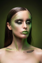 A beautiful slim topless girl with avant-garde green makeup close up portrait on a dark background....