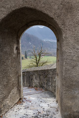 Obraz premium Through a stone arch we can see the mountains landscape on a cold winter day with fog and snow
