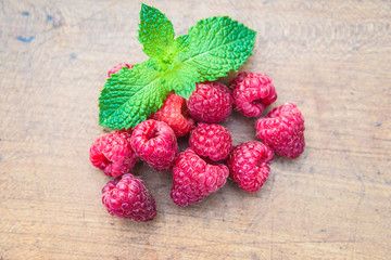 Heap of ripe red raspberries and mint leaves on wooden background