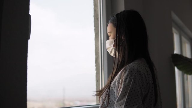 Sick teen of corona virus looking through the window and wearing mask protection and recovery from the illness quarantined in isolation in home