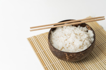 White rice in a coconut bowl on a white background. Minimalistic photo with rice and bamboo chopsticks.