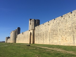 Fototapeta na wymiar outside ancient medieval wall, in a bright light with blue sky and green grass, walled french city of Aigues Mortes