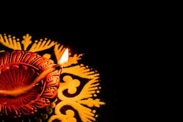 beautiful cropped earthen lamp in left corner with yellow rangoli on black background. diwali concept