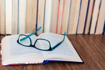 Open textbook, glasses, stack of old book on wooden table, education concept background, many books piles with copy space for text.