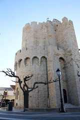 white stone church apse that looks like a fortress, free square with bare trees and blue sky,...