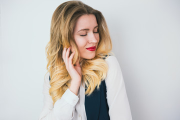 portrait of young blond beautiful woman with red lips wearing smart suit stands on isolated white background, looks sexy , style and beauty concept