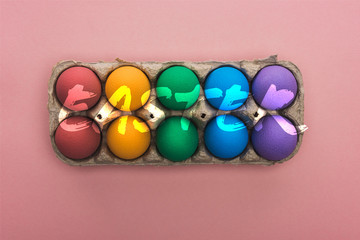 top view of painted eggs in cardboard box on pink background with Easter illustration