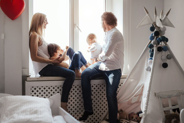 Obraz premium Happy smiling modern caucasian family playing and spending time in a bright white room near the window. Sunny day. Perfect parenting relationship. Parents of two cute boys.