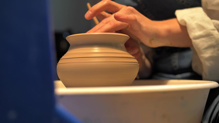 Fototapeta na wymiar Woman makes a pot on a pottery wheel in a workshop