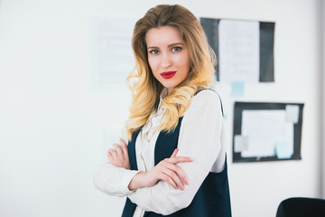 portrait of young blond beautiful businesswoman wearing smart suit stands in her bright office, work concept