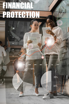 Concentrated African American And Asian Businesswomen With Digital Tablet And Documents Standing In Office With Multicultural Colleagues On Background, Financial Protection Illustration