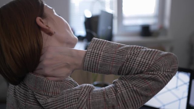 rear view tired woman feeling discomfort joint pain rubs cervical vertebra, girl massages her neck to relieve pain with fibromyalgia after prolonged work at computer in wrong position