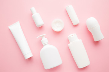 Different white toiletries on light pink table. Care about face, hands, legs and body skin. Women beauty products. Cosmetic pattern. Empty place for logo on bottles. Flat lay. Top down view.