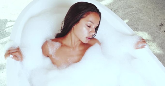 Top view of beautiful and sensual brunette woman relaxing in bathtub with foam - video in slow motion