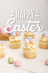 Selective focus of delicious easter cupcakes with painted quail eggs on grey background with happy Easter illustration