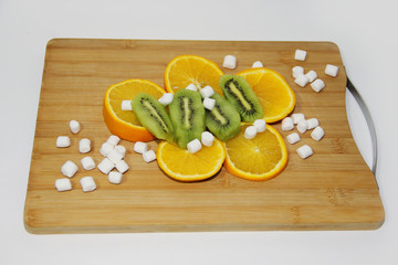 kiwi and orange fruit and marshmallows on a chopping Board