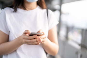 Fototapeta premium Young Asian woman using a touch screen smartphone while walking at the crowded place. Woman addicted social network all of the day. Woman talk to her friend by using smartphone. Copyspace in photo.