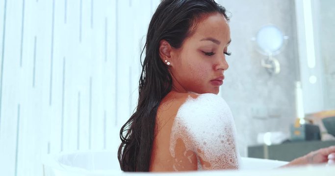 Beautiful and sensual brunette woman relaxing in bathtub with foam - video in slow motion