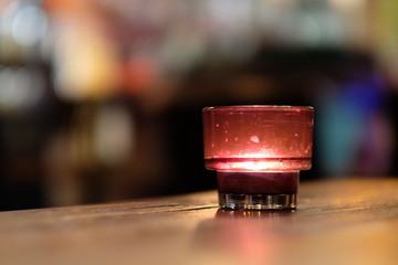 Close up candle light in red glass on wooden table in bar. Blur background