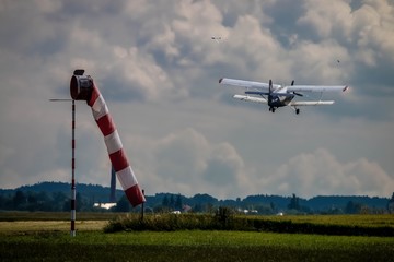 Photo of a small field airport with red and white windsock and a biplane taking off. Green field...