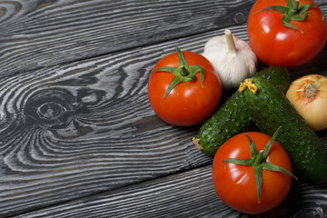 Tomatoes with green ponytails, onion and garlic head. Two green prickly cucumbers with yellow flowers. They lie on the surface of brushed pine boards.