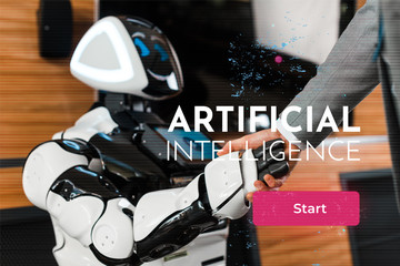 cropped view of businessman shaking hands with smiling robot in office, Artificial Intelligence...