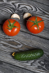 Tomato with a green ponytail, cucumber and garlic. They lie on the surface of brushed pine boards.