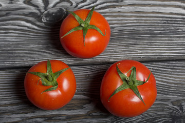Three red tomatoes with green ponytails lie on the surface of brushed pine boards.