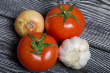 Tomato with green tail, cucumber, onions and garlic. They lie on the surface of brushed pine boards.