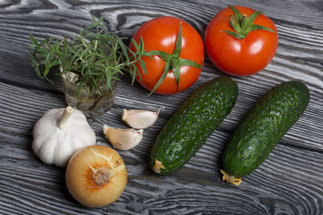 Tomatoes with green ponytails, onion, lemon and garlic head. Two green prickly cucumbers with yellow flowers. A glass with rosemary branches. They lie on the surface of brushed pine boards.