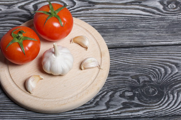 Red tomatoes with green ponytails and garlic on a cutting board. On the surface of brushed pine boards.