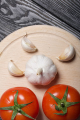 Red tomatoes with green ponytails and garlic on a cutting board. On the surface of brushed pine boards.