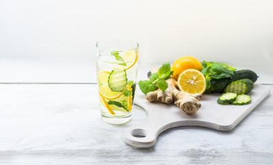 Detox Sassy water with lemon, cucumber, mint. A glass of clean, cool and fresh drink stands on a white wooden table with ingredients on board. Strengthening immunity, diet. Still life with copy space.