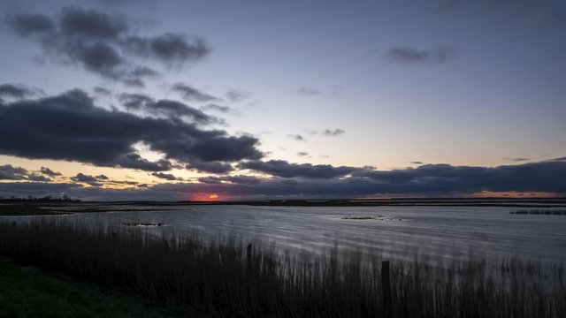 Time lapse of beautiful sunrise with orange sun star and massive clouds and a moore with reeds in the forground