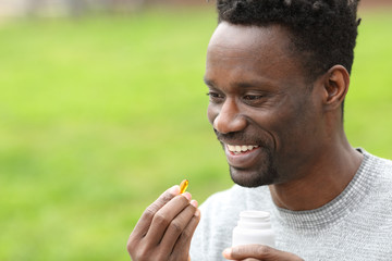 Happy black man taking vitamin pill in the park
