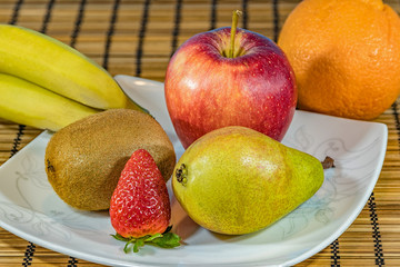 Fresh tropical and subtropical fruits in a large white dish. Wicker bamboo stand on the dining table. Close up, Selective focus