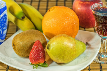 Fresh tropical and subtropical fruits in a large white dish. Cristal glass of red wine and blue and white carved crystal goblet on wicker bamboo stand on the dining table. Close up, Selective focus