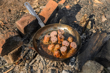 Grilled sausages are fried in a pan over a fire in a forest on a picnic