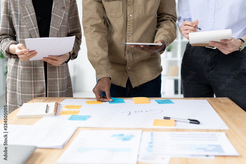 Poster close-up of unrecognizable multi-ethnic marketing team creating task plan to achieve goal in office