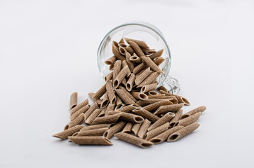 Pile of brown penne noodles, pasta, macaroni in glass cup isolated on white background. Pasta made...