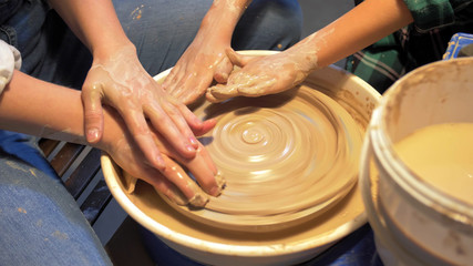 Woman and boy make plate on pottery wheel in workshop