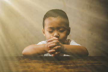 Little boy praying to God with hands held together with closed eyes