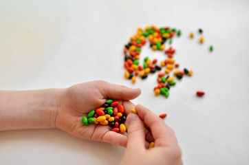  The child holds a lot of colorful sweets in his hands. Little pills.