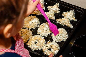 the girl greases baking oil to make a golden crust. little girl cooks in the kitchen. child hostess assistant. small daughter make prepare sweet pastries