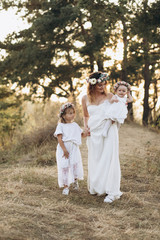 Happy elegant mother and her two beautiful daughters with flower wreaths in a nature at sunset