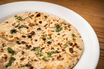 Close-up of traditional Indian chapatti (roti) garnished with coriander leafs served in white plate.
