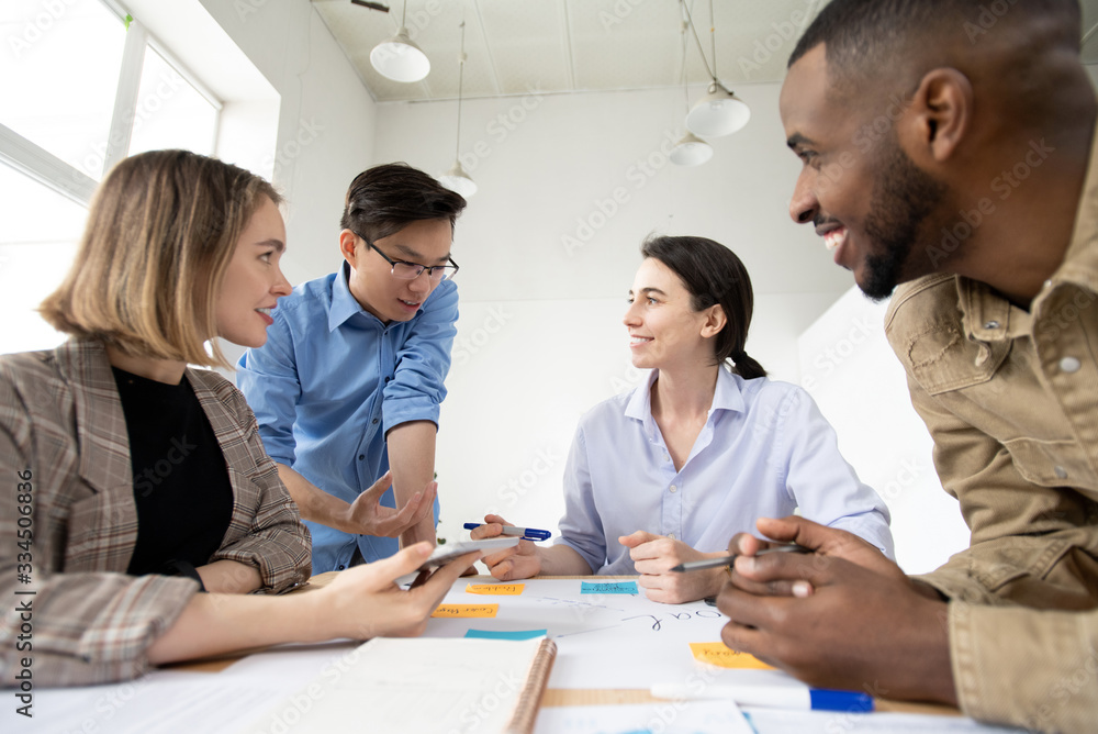 Poster Group of cheerful young multi-ethnic specialists adding notes on task board at meeting, active discussion of startup project