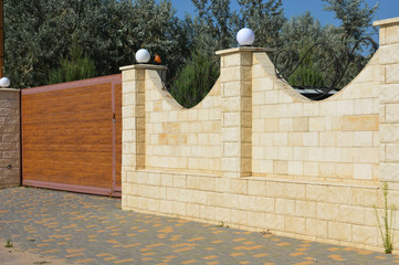 A brick fence with lanterns and wooden sliding gate in the paver block street.